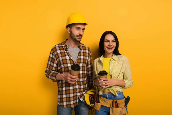 Smiling manual workers holding coffee to go on yellow — Stock Photo