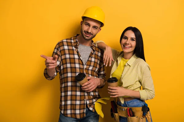 Professional manual workers with coffee to go pointing on yellow — Stock Photo
