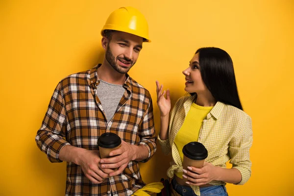 Positivi operai parlando e tenendo tazze con caffè per andare su giallo — Foto stock