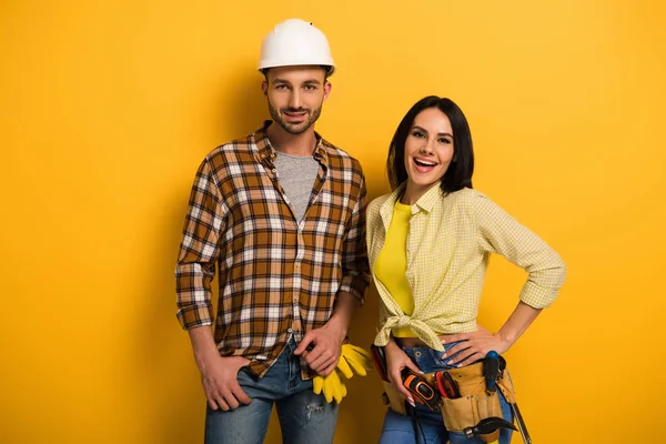 Trabajadores manuales sonrientes profesionales con cinturón de herramientas en amarillo - foto de stock