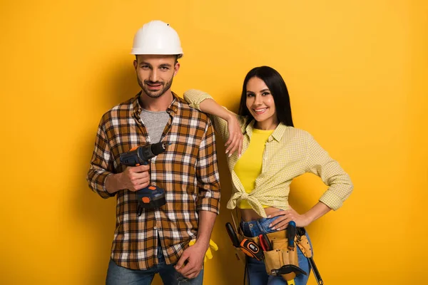 Travailleurs manuels souriants professionnels avec ceinture à outils tenant perceuse électrique sur jaune — Photo de stock