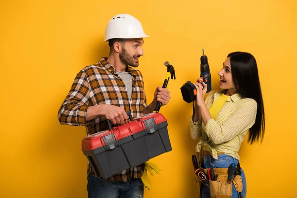 Heureux ouvriers tenant boîte à outils et perceuse électrique sur jaune — Photo de stock