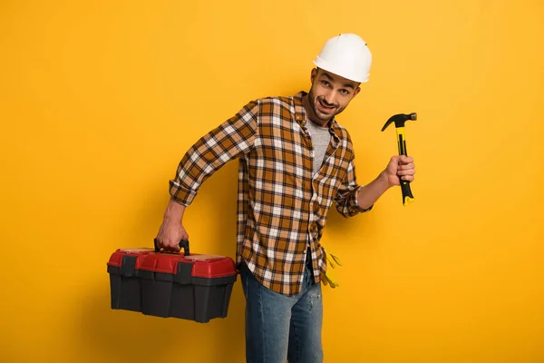 Lächelnder Arbeiter mit Werkzeugkiste und Hammer auf gelb — Stockfoto