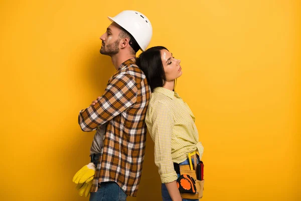 Tired manual workers standing back to back on yellow — Stock Photo