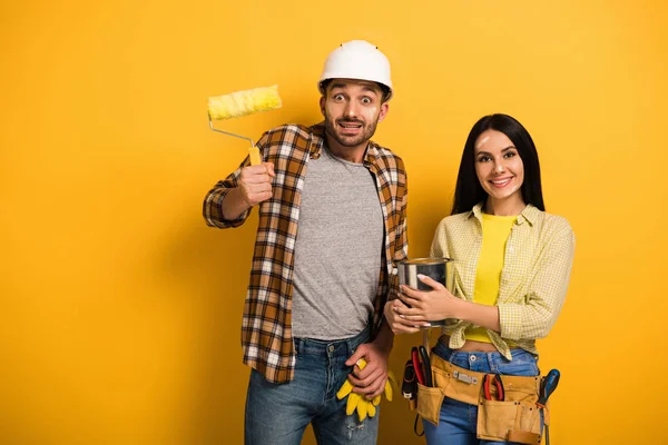 Trabajadores manuales emocionales con rodillo de pintura y lata de pintura en amarillo - foto de stock