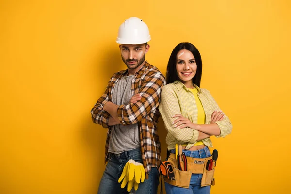 Confident smiling manual workers with crossed arms on yellow — Stock Photo