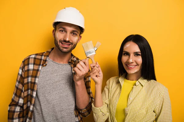Trabalhadores manuais sorridentes com pincéis de pintura em amarelo — Fotografia de Stock