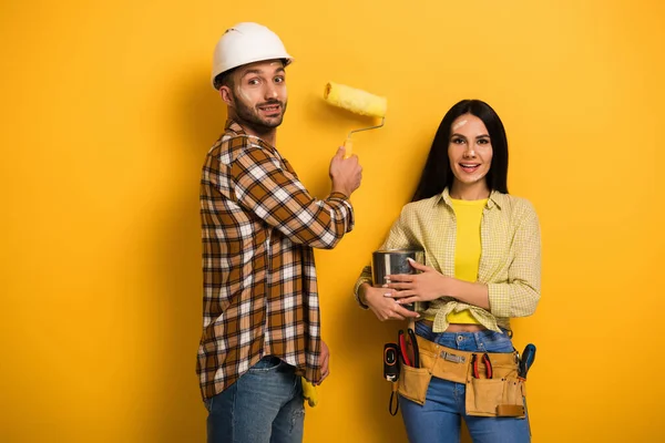 Trabajadores manuales sonrientes con rodillo de pintura y lata de pintura en amarillo - foto de stock