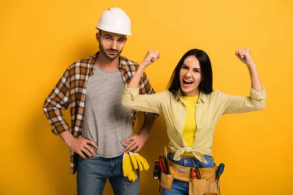 Trabalhador manual feminino animado bem sucedido com as mãos para cima perto colega de trabalho em amarelo — Fotografia de Stock