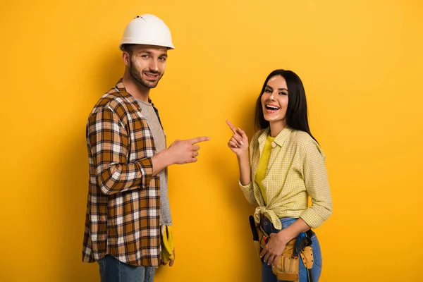 Laughing manual workers pointing at each other on yellow — Stock Photo