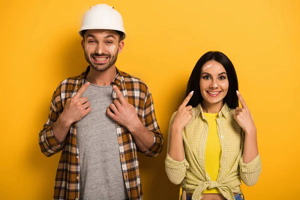 Trabajadores manuales felices apuntándose a sí mismos en amarillo - foto de stock