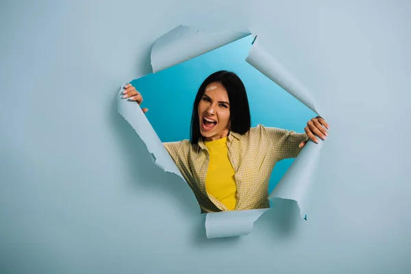 Angry workwoman with dirty face in paint yelling in torn paper, isolated on blue — Stock Photo