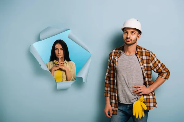 Trabalhador pensativo em capacete e mulher em papel rasgado, isolado em azul — Fotografia de Stock