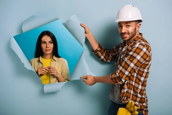 Verwirrter Arbeiter mit Helm und Frau in zerrissenem Papier, isoliert auf blauem Grund — Stockfoto