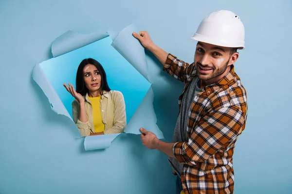 Workman in helmet and frustrated woman in torn paper, isolated on blue — Stock Photo