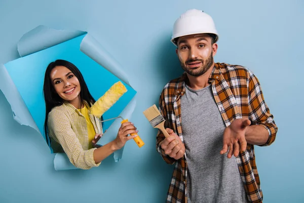 Operaio con pennello e donna con rullo di vernice in carta strappata, isolato su blu — Foto stock