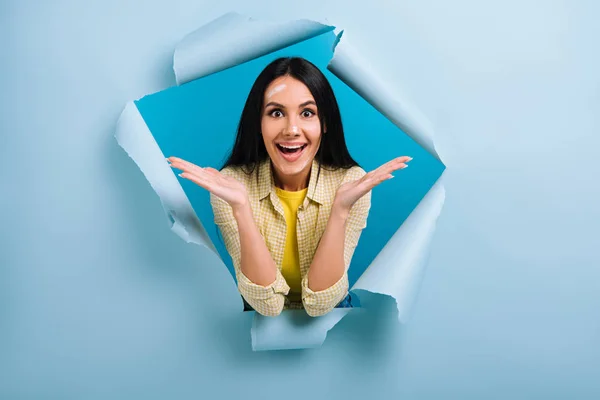 Beautiful excited workwoman with dirty face in paint standing in torn paper, isolated on blue — Stock Photo