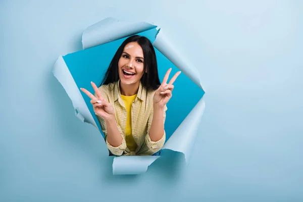 Femme de travail excitée avec le visage sale dans la peinture montrant des signes de victoire en papier déchiré, isolé sur bleu — Photo de stock