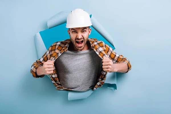 Angry foreman in yelling in torn paper, isolated on blue — Stock Photo