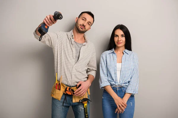 Felizes trabalhadores manuais segurando broca elétrica em cinza — Fotografia de Stock