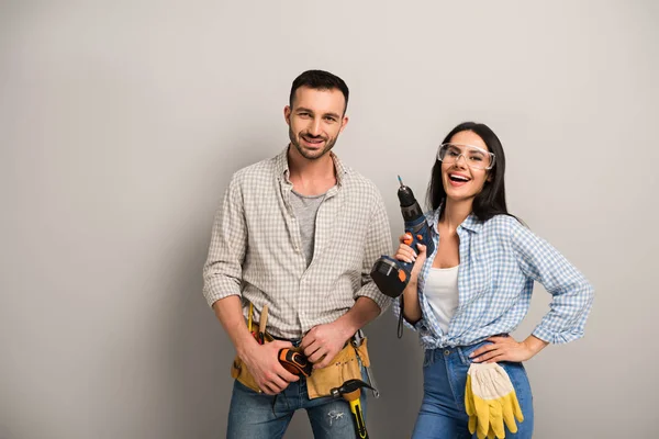 Excited manual workers holding electric drill on grey — Stock Photo