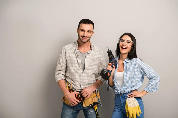 Trabajadores manuales excitados sosteniendo taladro eléctrico en gris — Stock Photo