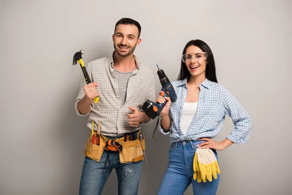 Travailleurs manuels excités tenant marteau et perceuse électrique sur gris — Photo de stock