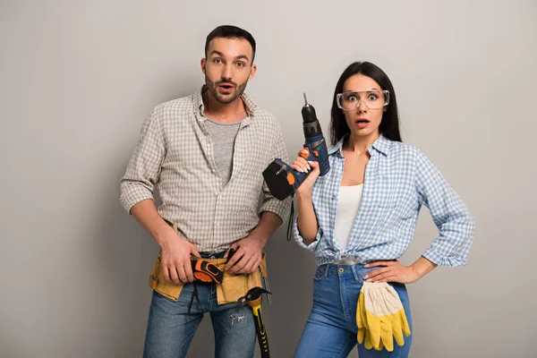 Shocked manual workers holding electric drill on grey — Stock Photo