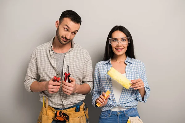 Emotional manual workers holding pliers and paint roller on grey — Stock Photo