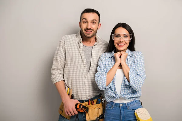 Travailleurs manuels excités avec ceinture à outils et lunettes sur gris — Photo de stock