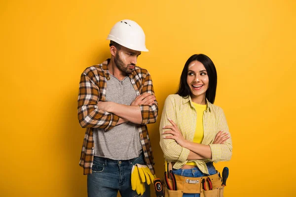 Sonriente trabajadora manual y obrero ofendido con brazos cruzados en amarillo - foto de stock