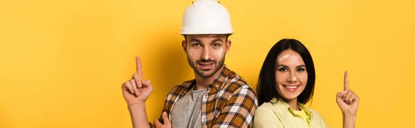 Tiro panorâmico de trabalhadores manuais alegres que têm ideia e apontando para cima no amarelo — Fotografia de Stock