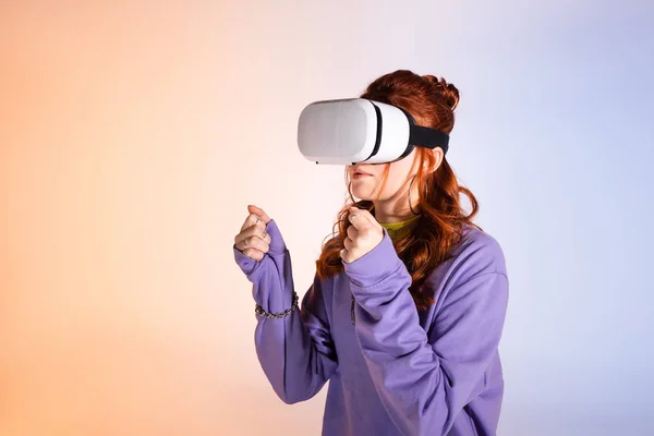 Chica adolescente concentrada usando auriculares de realidad virtual, en púrpura y beige - foto de stock