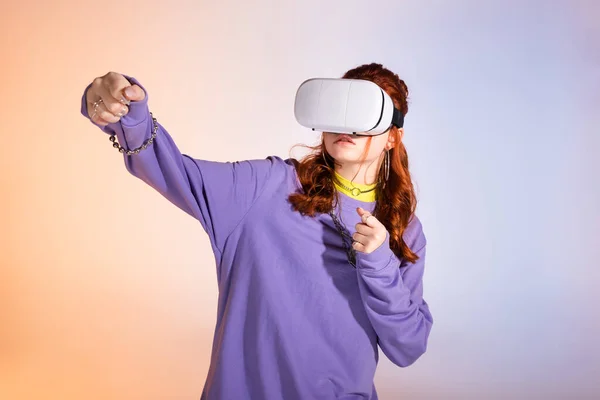 Menina adolescente emocional gesticulando e usando fone de ouvido realidade virtual, em roxo e bege — Fotografia de Stock