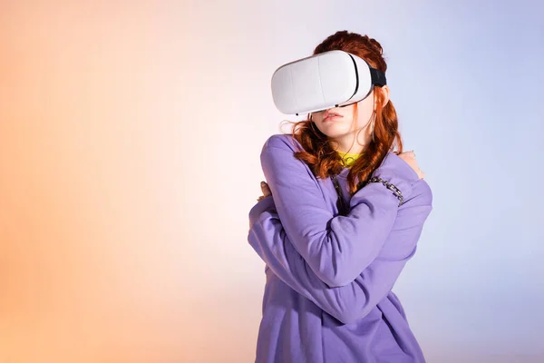 Chica adolescente triste usando auriculares de realidad virtual, en púrpura y beige - foto de stock
