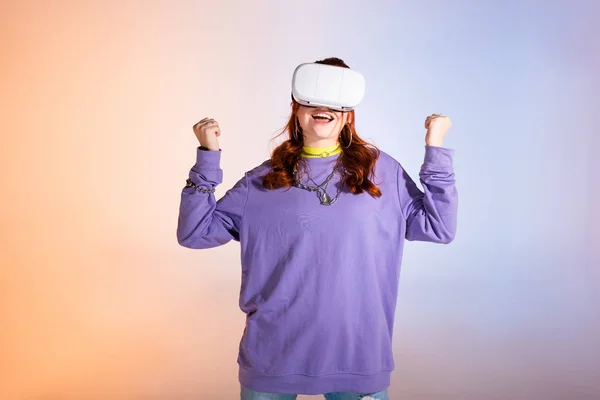 Excited teen girl gesturing and using virtual reality headset, on purple and beige — Stock Photo
