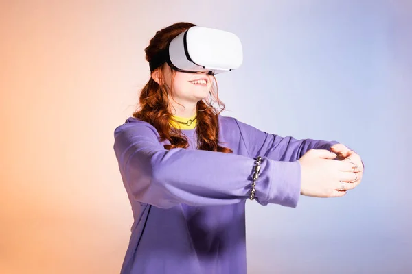 Feliz adolescente hembra abrazando y usando auriculares de realidad virtual, en púrpura y beige - foto de stock