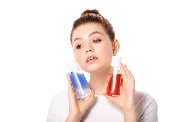 Belle adolescente tenant deux bouteilles avec des démaquillants rouges et bleus, isolée sur blanc — Photo de stock