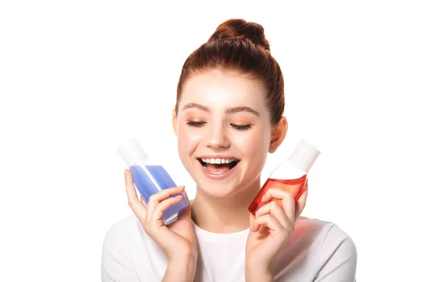 Excitada adolescente sosteniendo dos botellas con removedores de maquillaje rojo y azul, aislado en blanco - foto de stock