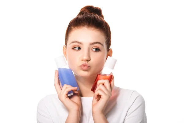 Pensativo adolescente sosteniendo dos botellas con removedores de maquillaje rojo y azul, aislado en blanco - foto de stock