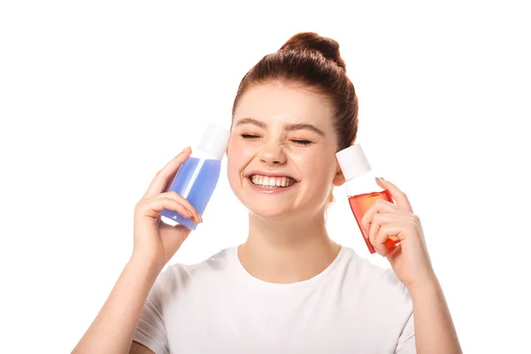 Adolescente emocional sosteniendo dos botellas con removedores de maquillaje rojo y azul, aislado en blanco - foto de stock