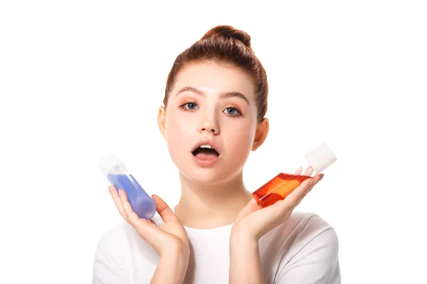 Surprised teenager holding two bottles with red and blue makeup removers, isolated on white — Stock Photo