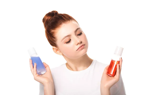 Menina adolescente pensativo segurando duas garrafas com removedores de maquiagem vermelho e azul, isolado em branco — Fotografia de Stock