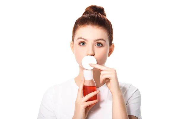 Surprised teenager with clean skin holding cotton sponge and bottle with red makeup remover, isolated on white — Stock Photo