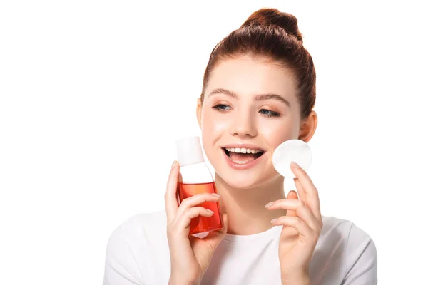Aufgeregten weiblichen Teenager mit sauberer Haut hält Baumwollschwamm und Flasche mit rotem Make-up-Entferner, isoliert auf weiß — Stockfoto