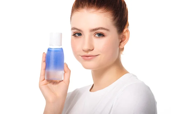 Bela menina adolescente sorridente com pele limpa segurando garrafa com removedor de maquiagem azul, isolado no branco — Fotografia de Stock