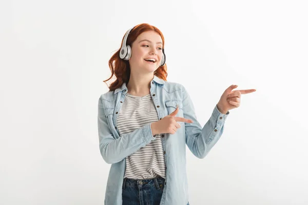 Збуджена дівчина-підліток слухає музику з навушниками і вказує ізольовано на білому — стокове фото