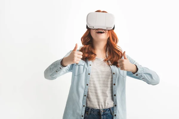 Adolescente pelirroja emocionada mostrando pulgares hacia arriba y el uso de auriculares de realidad virtual, aislado en blanco - foto de stock