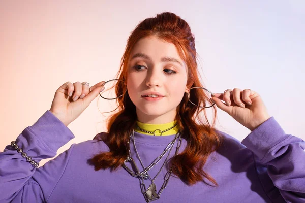 Beautiful smiling redhead teen girl holding earrings, on purple and beige — Stock Photo