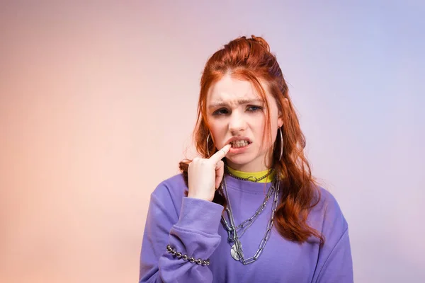 Preocupado nervioso mujer adolescente mordiendo dedo, en púrpura y beige - foto de stock